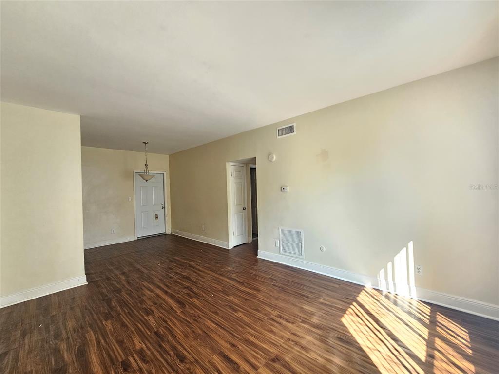 An empty living room features wood-look flooring, beige walls, a white front door, and a doorway — 7611 PAULA DRIVE UNIT 5, TAMPA, FL