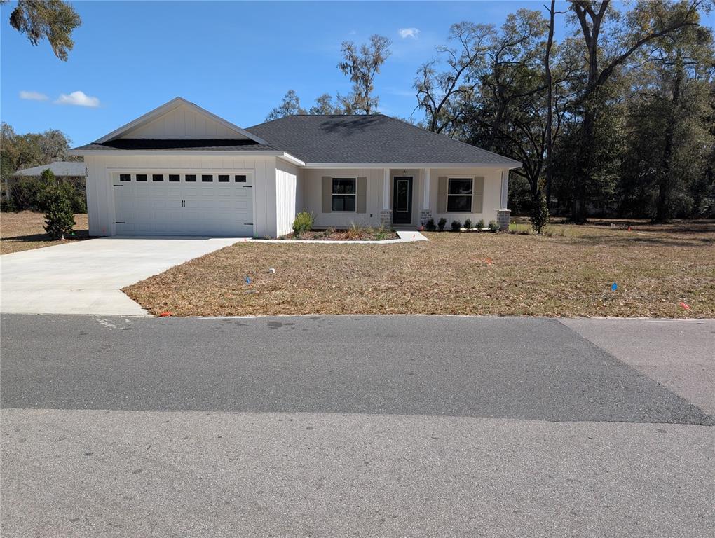 A single-story white house with a two-car garage and a dark shingled roof — 1303 NE 23RD AVENUE, OCALA, FL