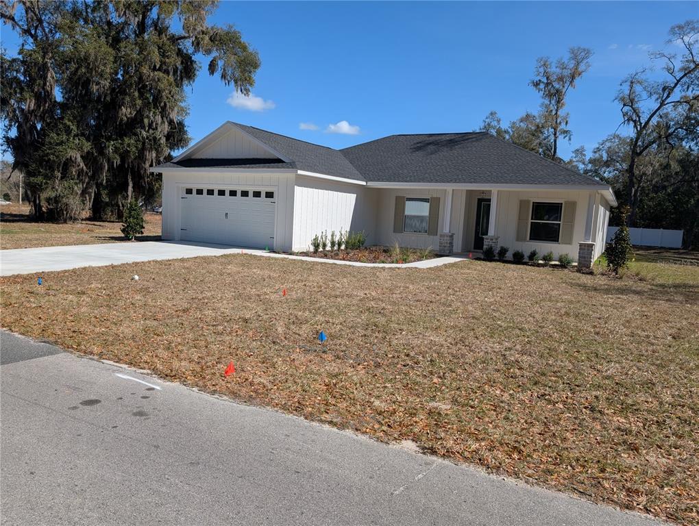 A single-story white house with a two-car garage sits on a grassy lot — 1303 NE 23RD AVENUE, OCALA, FL