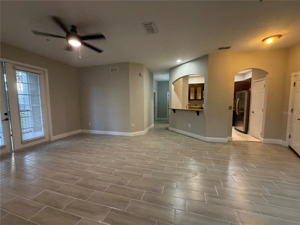 A living room features light-colored wood-look tile flooring, a ceiling fan, and a kitchen pass-through — 3001 LAUREL RUN LANE UNIT 104, KISSIMMEE, FL