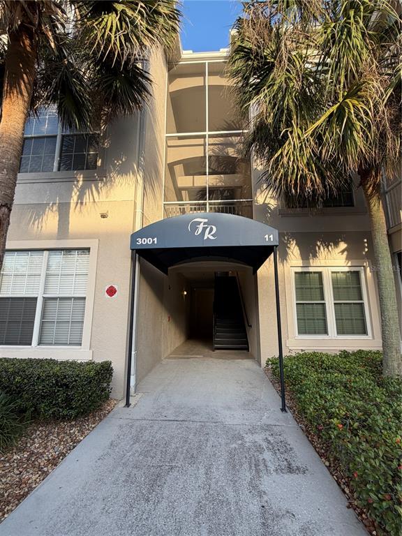 An exterior view of a multi-story apartment building entrance with a covered walkway and stairs — 3001 LAUREL RUN LANE UNIT 104, KISSIMMEE, FL