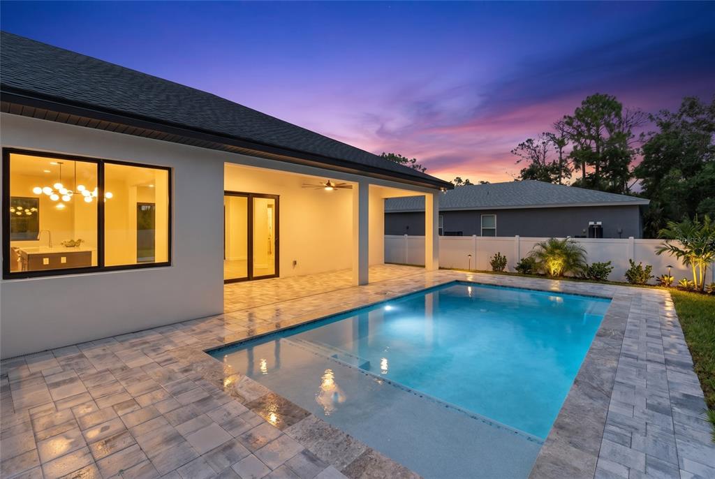 A backyard swimming pool with a paved deck sits beside a house with a covered patio — 150 HEATHER STREET, PORT CHARLOTTE, FL