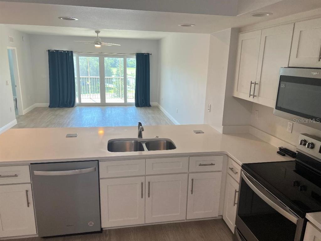 A kitchen with white cabinets and stainless steel appliances overlooks an open living area — 960 STARKEY ROAD UNIT 10305, LARGO, FL
