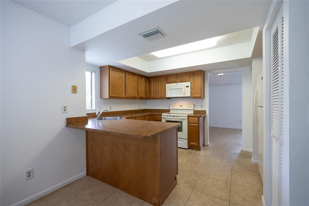 A kitchen features wood cabinets, laminate countertops, white appliances, and light-colored tile flooring — 9 SOUTHBURY COURT UNIT 9, PALM COAST, FL