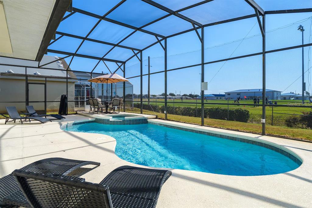 A screened-in pool and hot tub area with lounge chairs overlooking a grassy field — 434 HENLEY CIR, DAVENPORT, FL