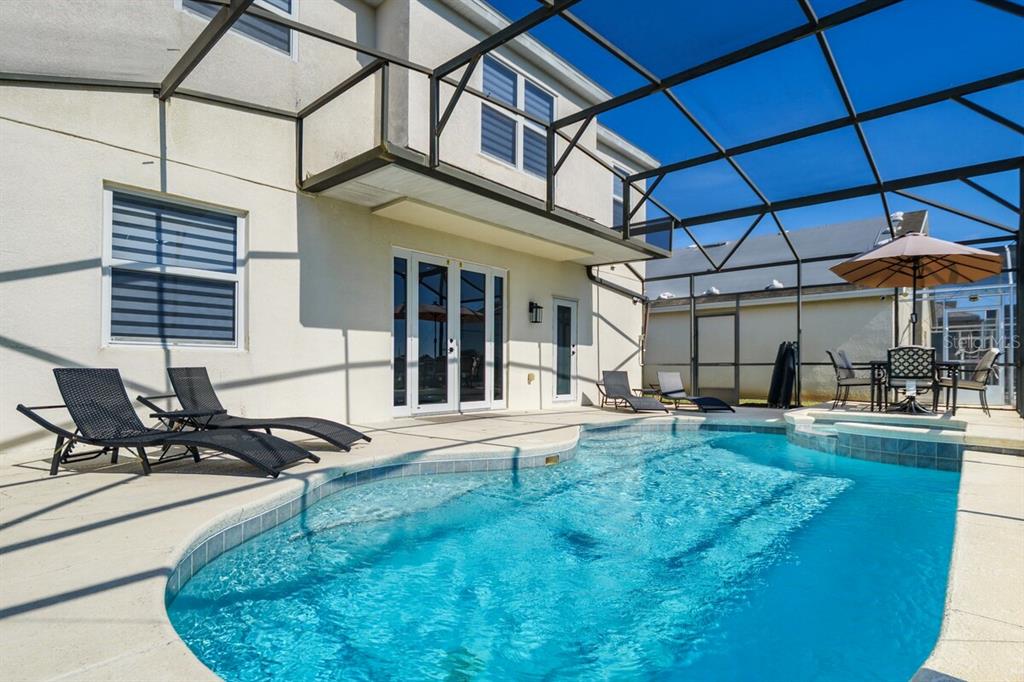 A swimming pool with a screened-in patio and lounge chairs sits behind a two-story house — 434 HENLEY CIR, DAVENPORT, FL