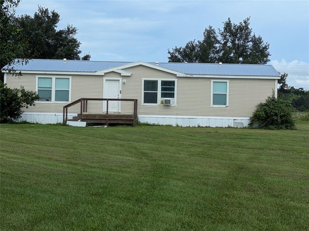 A single-story manufactured home with light siding, a metal roof, and a wooden front deck — 1291 NE HANSEL AVENUE, ARCADIA, FL