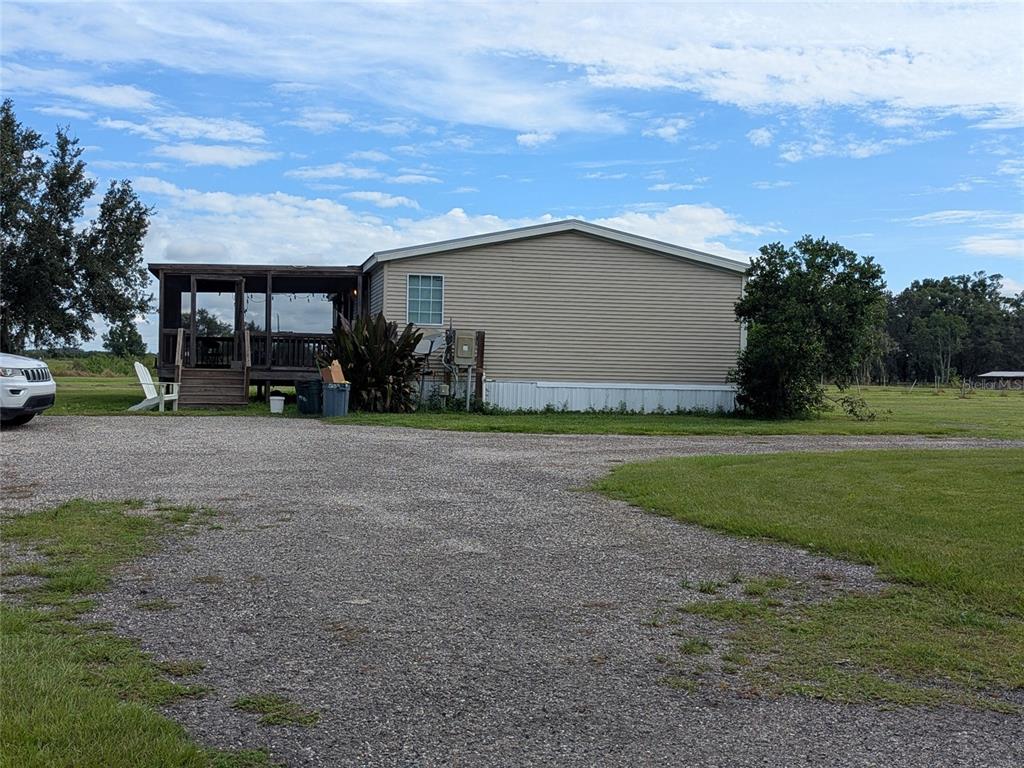 A tan manufactured home features a screened-in porch and a gravel driveway — 1291 NE HANSEL AVENUE, ARCADIA, FL