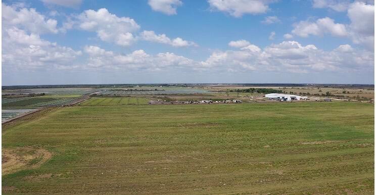 An aerial view shows a large, flat, grassy field with a distant industrial building — 3859 NE 144th Street, Okeechobee FL 34972, OKEECHOBEE, FL