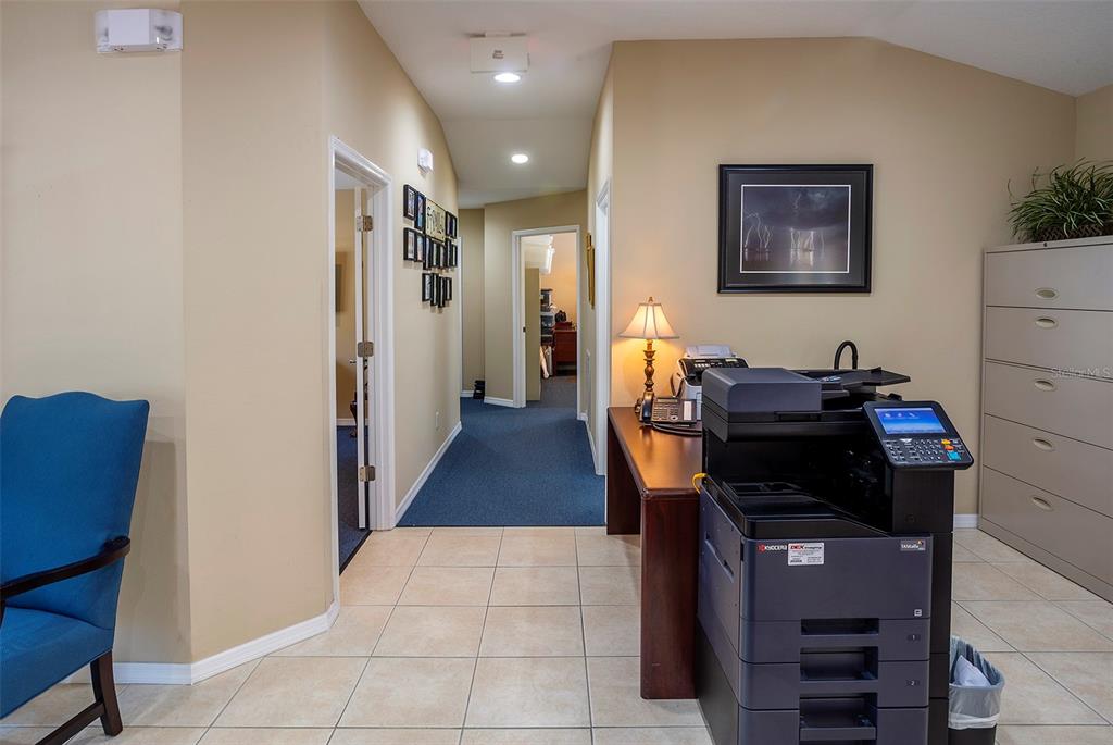 An office area features a large printer, a desk with a lamp, and a hallway — 310 WILDWOOD WAY, BELLEAIR, FL