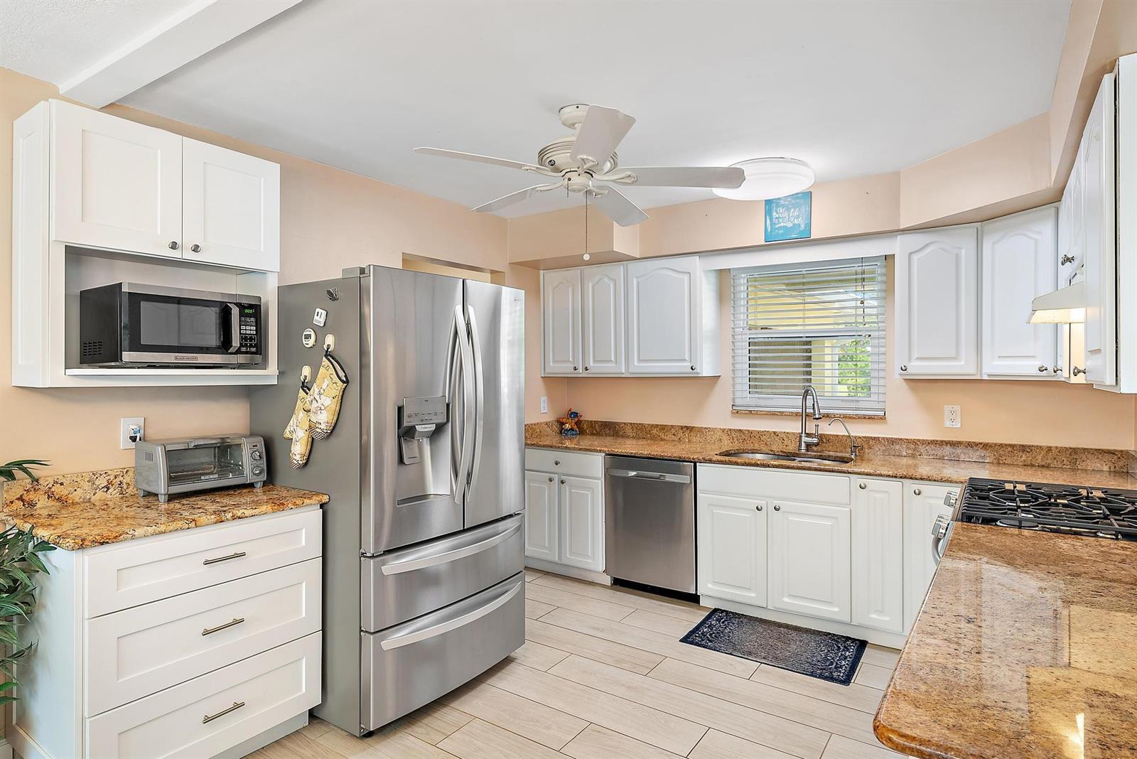 A kitchen features white cabinets, stainless steel appliances, granite countertops, and light-colored tile flooring — 1211 Dolphin Road, Riviera Beach FL 33404, RIVIERA BEACH, FL