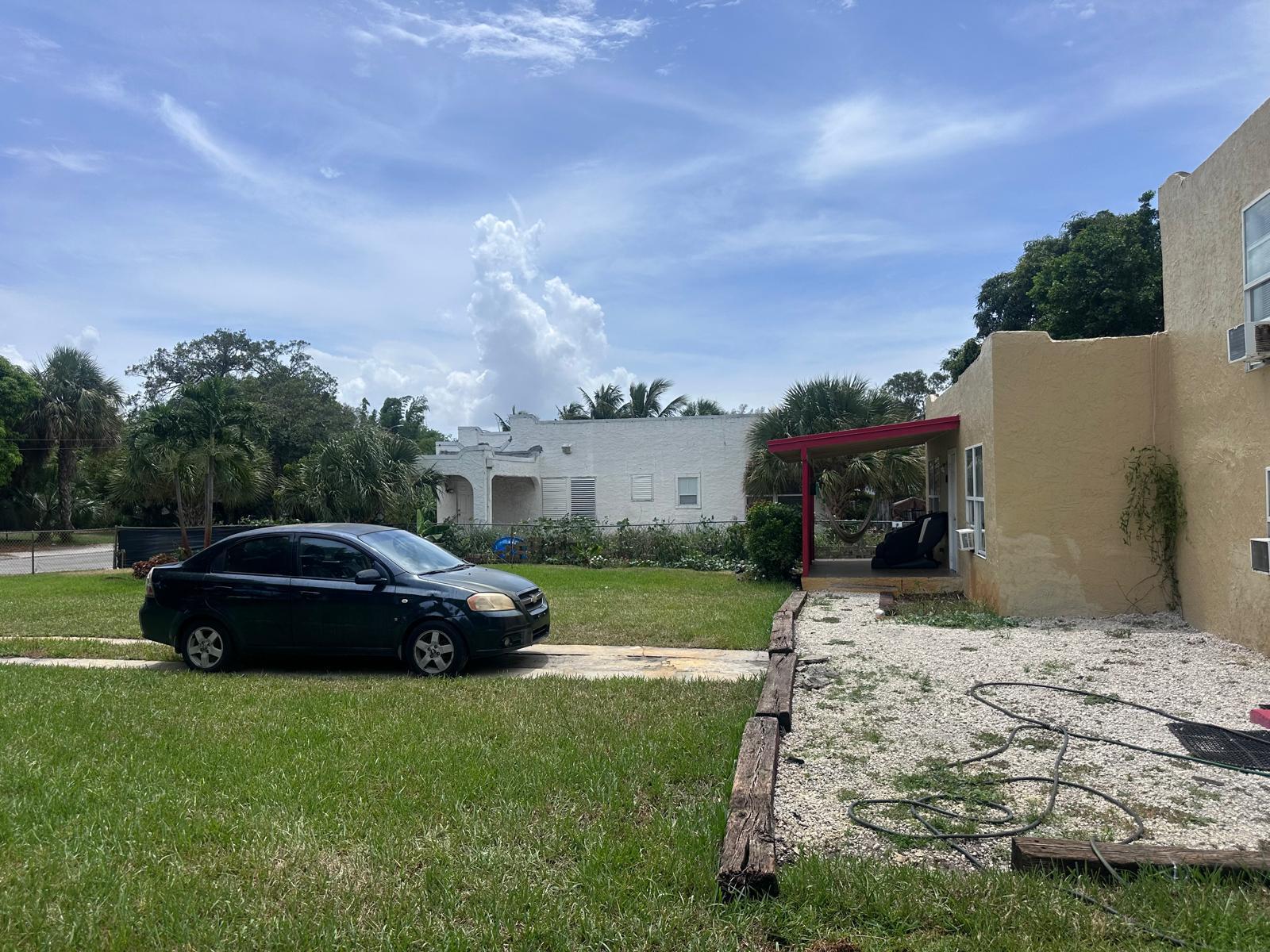 A black sedan is parked on a driveway next to a tan house with a porch — 637 46th Street, West Palm Beach FL 33407, WEST PALM BEACH, FL