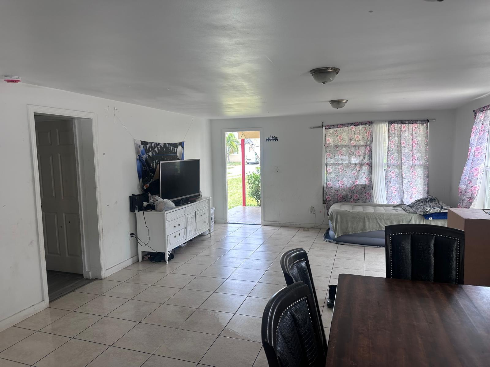 A living and dining area features white tile floors, a television on a dresser, and curtains — 637 46th Street, West Palm Beach FL 33407, WEST PALM BEACH, FL