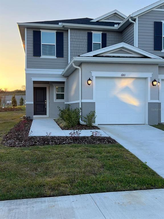 A two-story townhouse exterior features a white garage door, dark front door, and gray siding — 680 STONEY POINT CIRCLE, DAVENPORT, FL