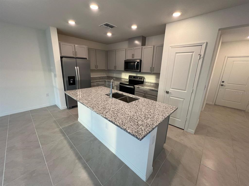 A kitchen features gray cabinets, granite countertops, a central island with a sink, and tile flooring — 680 STONEY POINT CIRCLE, DAVENPORT, FL