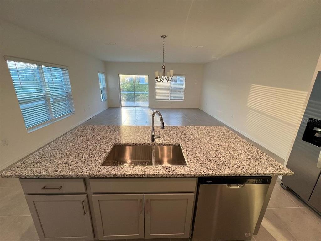 A kitchen island with a granite countertop and stainless steel sink overlooks an open living area — 680 STONEY POINT CIRCLE, DAVENPORT, FL