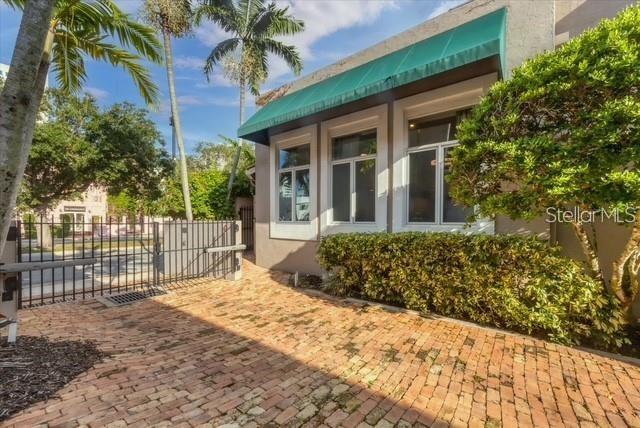 A brick courtyard leads to a building exterior with large windows and a green awning — 200 COCOANUT AVENUE UNIT 7, SARASOTA, FL
