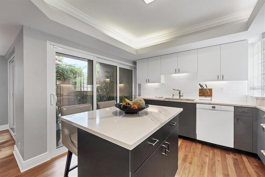 A modern kitchen features a central island, white upper cabinets, dark lower cabinets, and sliding doors — 200 COCOANUT AVENUE UNIT 7, SARASOTA, FL