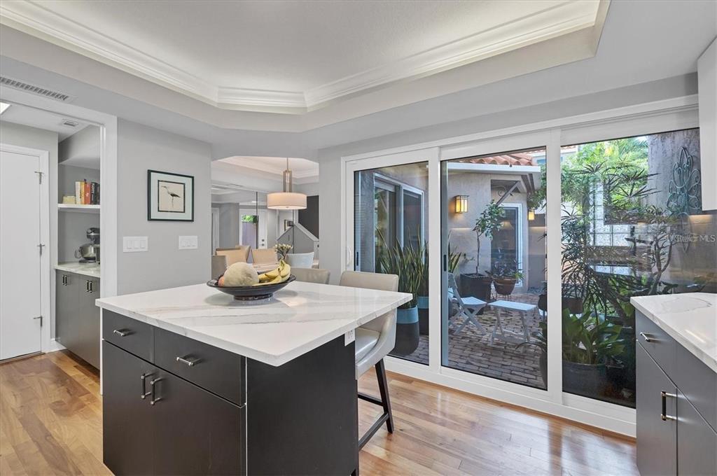 A kitchen island with a white countertop sits before sliding glass doors opening to a patio — 200 COCOANUT AVENUE UNIT 7, SARASOTA, FL