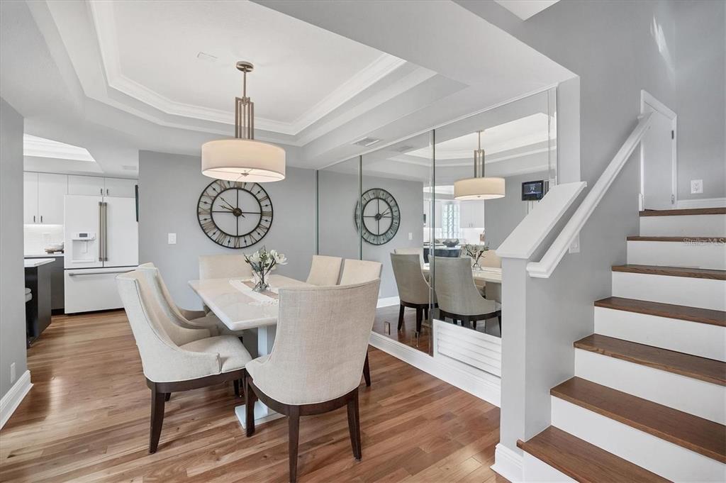 A dining room with a white table, upholstered chairs, a mirrored wall, and wooden stairs — 200 COCOANUT AVENUE UNIT 7, SARASOTA, FL