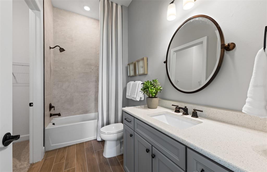 A bathroom features a gray vanity, a round mirror, and a tub-shower combination — 26641 BERING DRIVE, ENGLEWOOD, FL