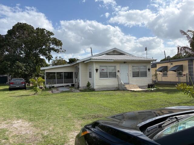 A single-story house with light-colored siding, a metal roof, and an attached screened-in porch — 522 E Ventura Avenue, Clewiston FL 33440, CLEWISTON, FL