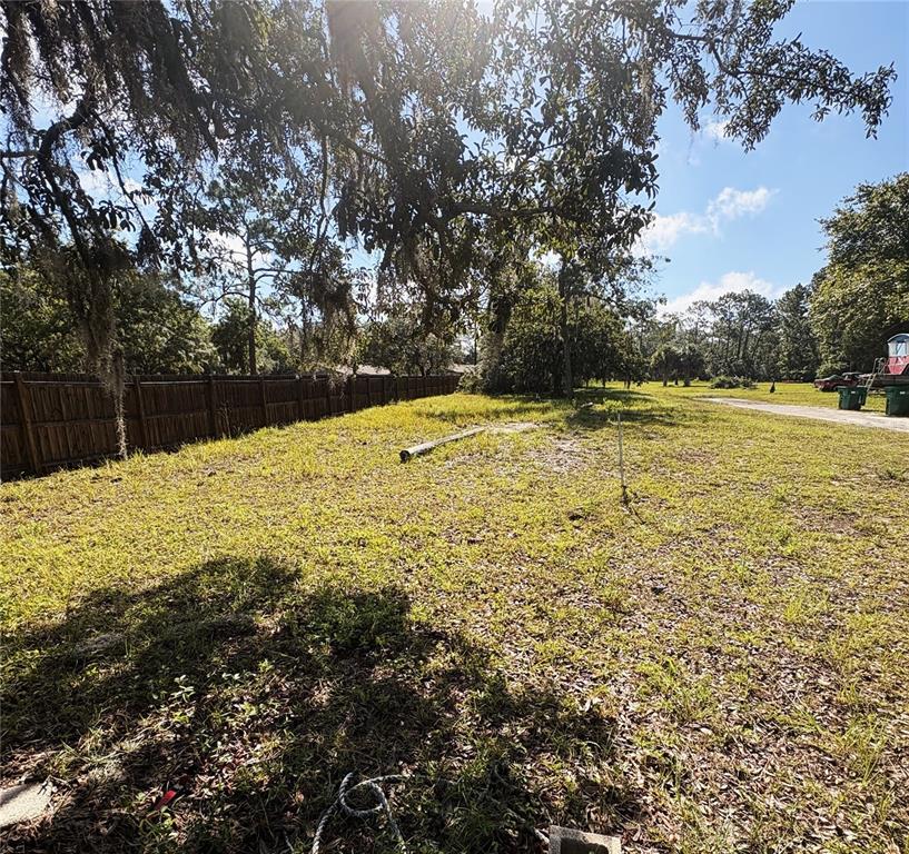 A grassy, partially shaded lot features a wooden fence along the left side — 8999 S SUNCOAST BOULEVARD, HOMOSASSA, FL