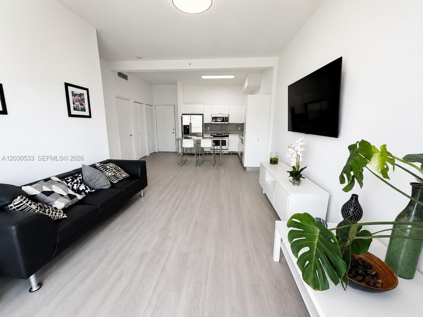 This open-concept living room features light wood-look flooring, a black sofa, and a kitchen area — 234 NE 3rd St # 905, Miami FL 33132, MIAMI, FL
