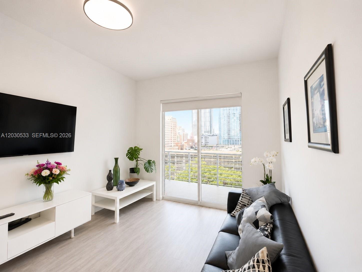 A living room features a black sofa, white media console, and a balcony with city views — 234 NE 3rd St # 905, Miami FL 33132, MIAMI, FL