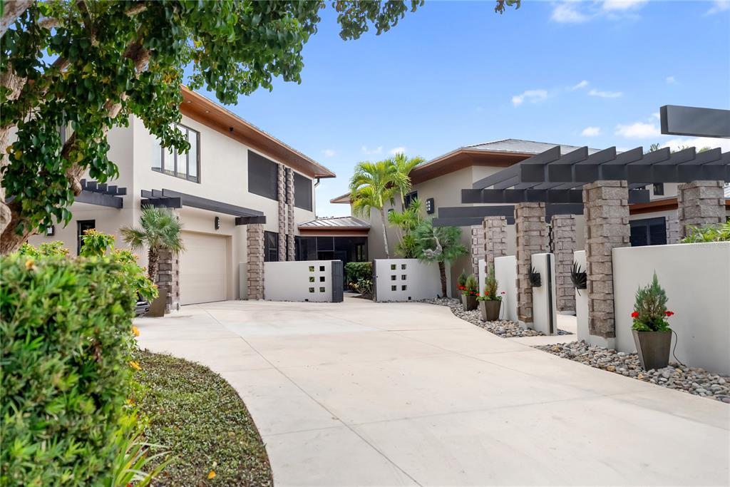 A concrete driveway leads to a modern two-story house with stone pillars and wooden pergolas — 1804 N LAKE SHORE DRIVE, SARASOTA, FL