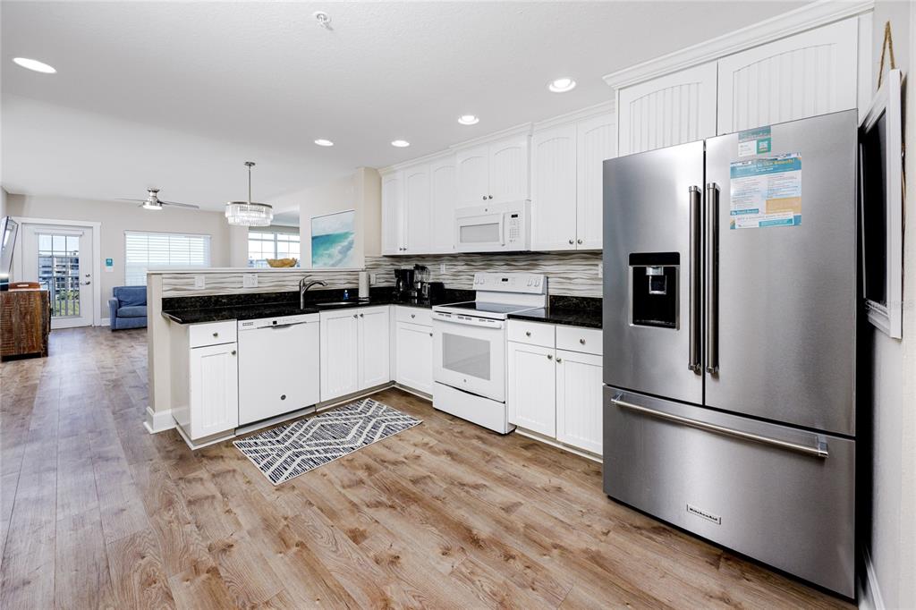 A kitchen features white cabinets, black countertops, stainless steel appliances, and wood-look flooring — 399 2ND STREET UNIT 718, INDIAN ROCKS BEACH, FL