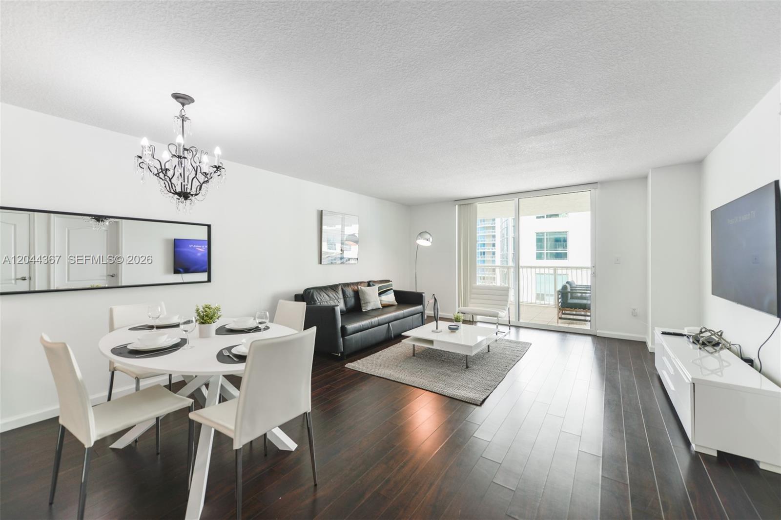 A living and dining area features dark wood floors, white furniture, and a balcony view — 1200 Brickell Bay Dr # 3614, Miami FL 33131, MIAMI, FL