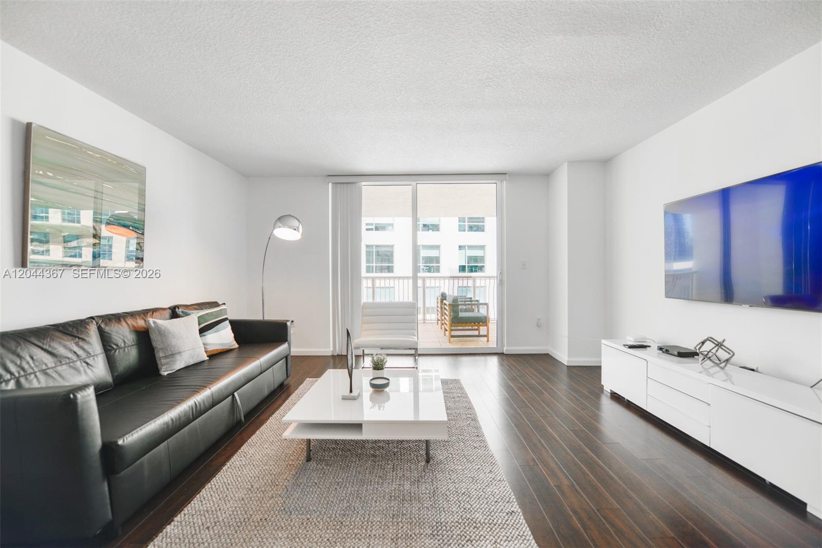 A living room features a black leather sofa, white coffee table, and dark wood floors — 1200 Brickell Bay Dr # 3614, Miami FL 33131, MIAMI, FL