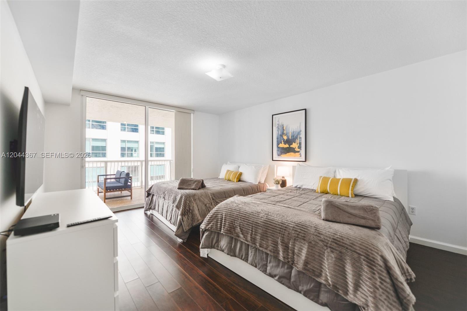 A bedroom features two beds, dark wood flooring, and a balcony with outdoor seating — 1200 Brickell Bay Dr # 3614, Miami FL 33131, MIAMI, FL