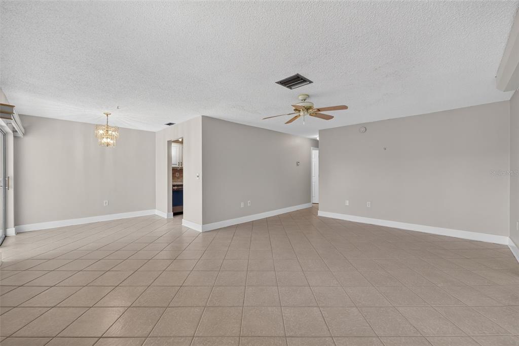 An empty living and dining area features beige tile flooring, light gray walls, and a ceiling fan — 1211 11TH CIRCLE SE, LARGO, FL
