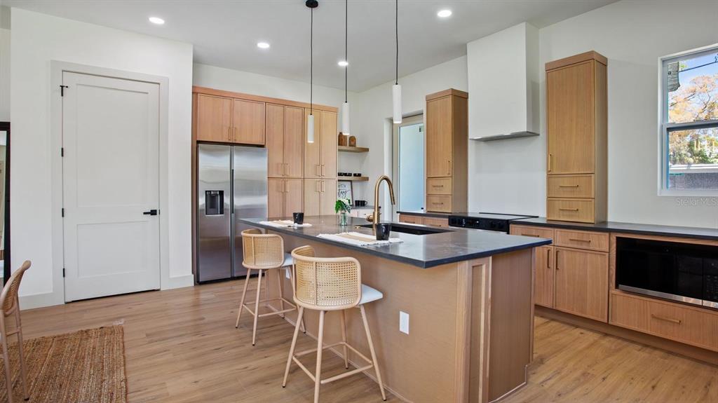 A modern kitchen features light wood cabinetry, a dark island countertop, and two rattan stools — 1505 W ARCH STREET UNIT 2, TAMPA, FL