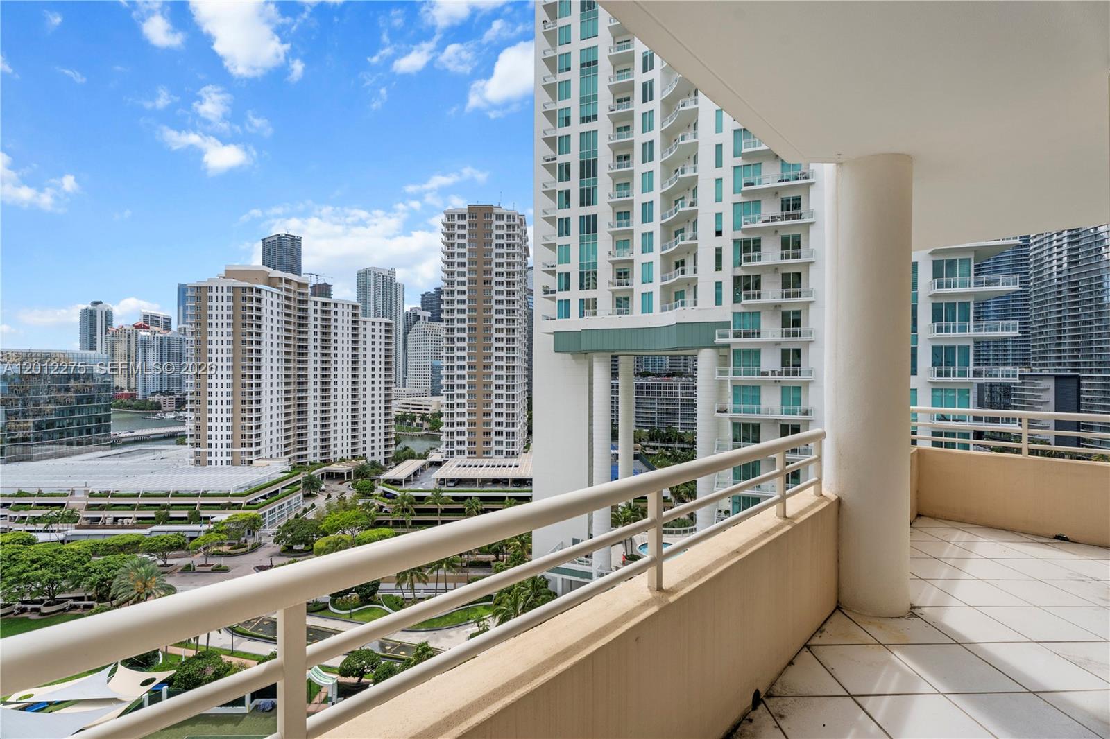 A high-rise balcony overlooks a city skyline with multiple tall residential buildings and greenery — 888 Brickell Key Dr # 1702, Miami FL 33131, MIAMI, FL