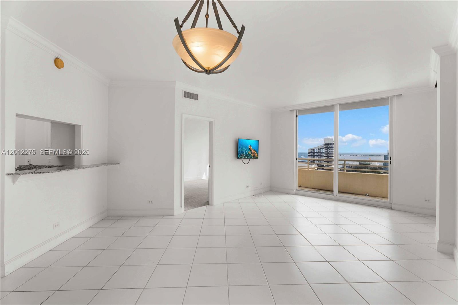 A bright, white-tiled living room features a hanging light fixture, a wall-mounted television, and a balcony — 888 Brickell Key Dr # 1702, Miami FL 33131, MIAMI, FL