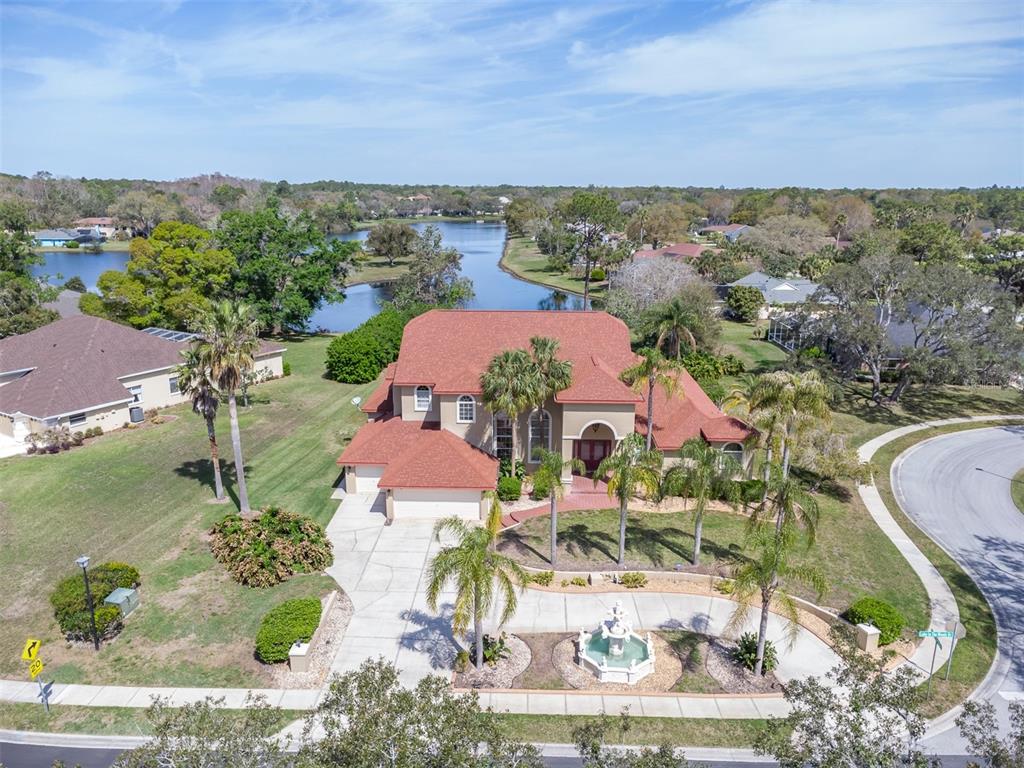 An aerial view shows a large house with a red roof, fountain, and circular driveway — 4404 LAKE IN THE WOODS DRIVE, SPRING HILL, FL
