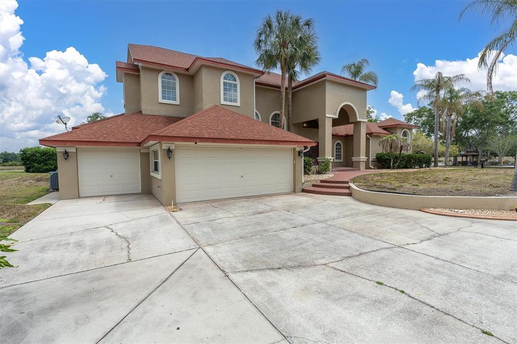 A two-story house with a three-car garage, tan stucco exterior, and a red shingled roof — 4404 LAKE IN THE WOODS DRIVE, SPRING HILL, FL