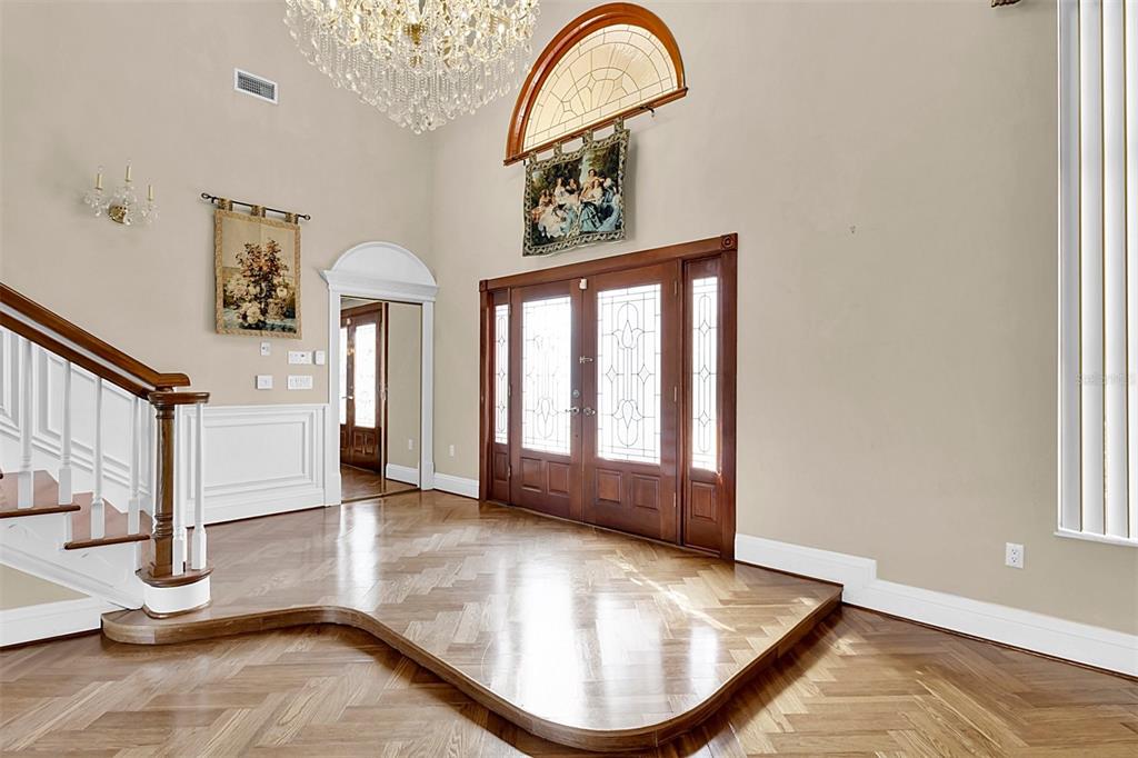 An entryway features a raised herringbone wood floor, a grand chandelier, and a double-door entrance — 4404 LAKE IN THE WOODS DRIVE, SPRING HILL, FL
