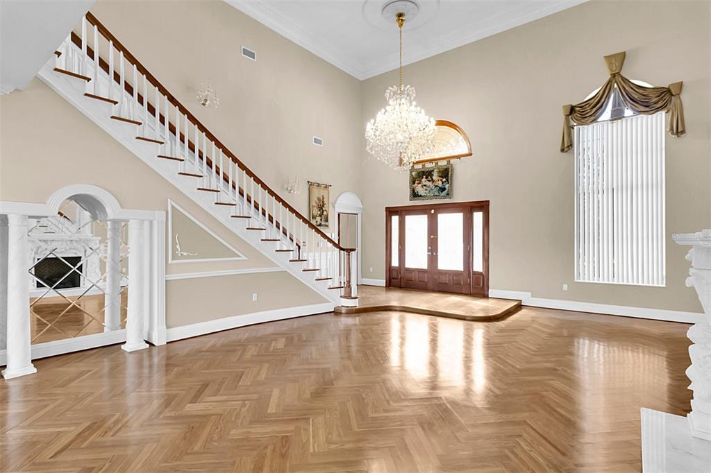 A grand foyer features a herringbone wood floor, a sweeping staircase, and a crystal chandelier — 4404 LAKE IN THE WOODS DRIVE, SPRING HILL, FL