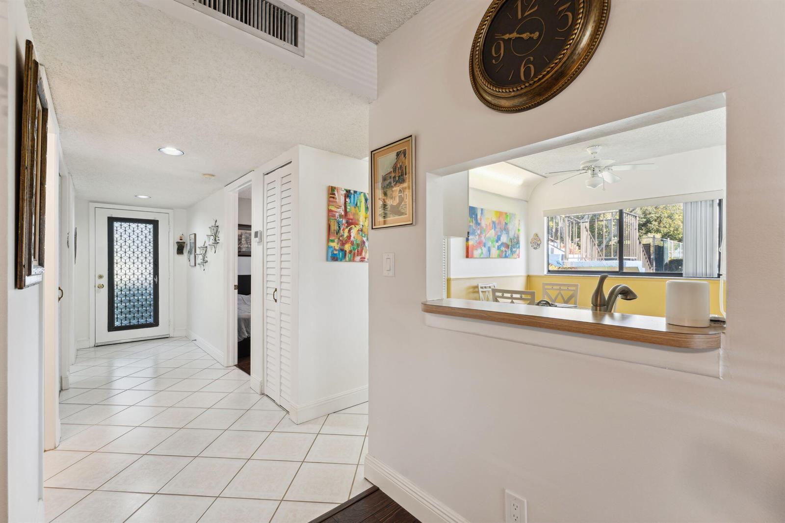 A hallway with white tile floors leads to an entryway, featuring a kitchen pass-through window — 15301 Pembridge Avenue # 43, Delray Beach FL 33484, DELRAY BEACH, FL