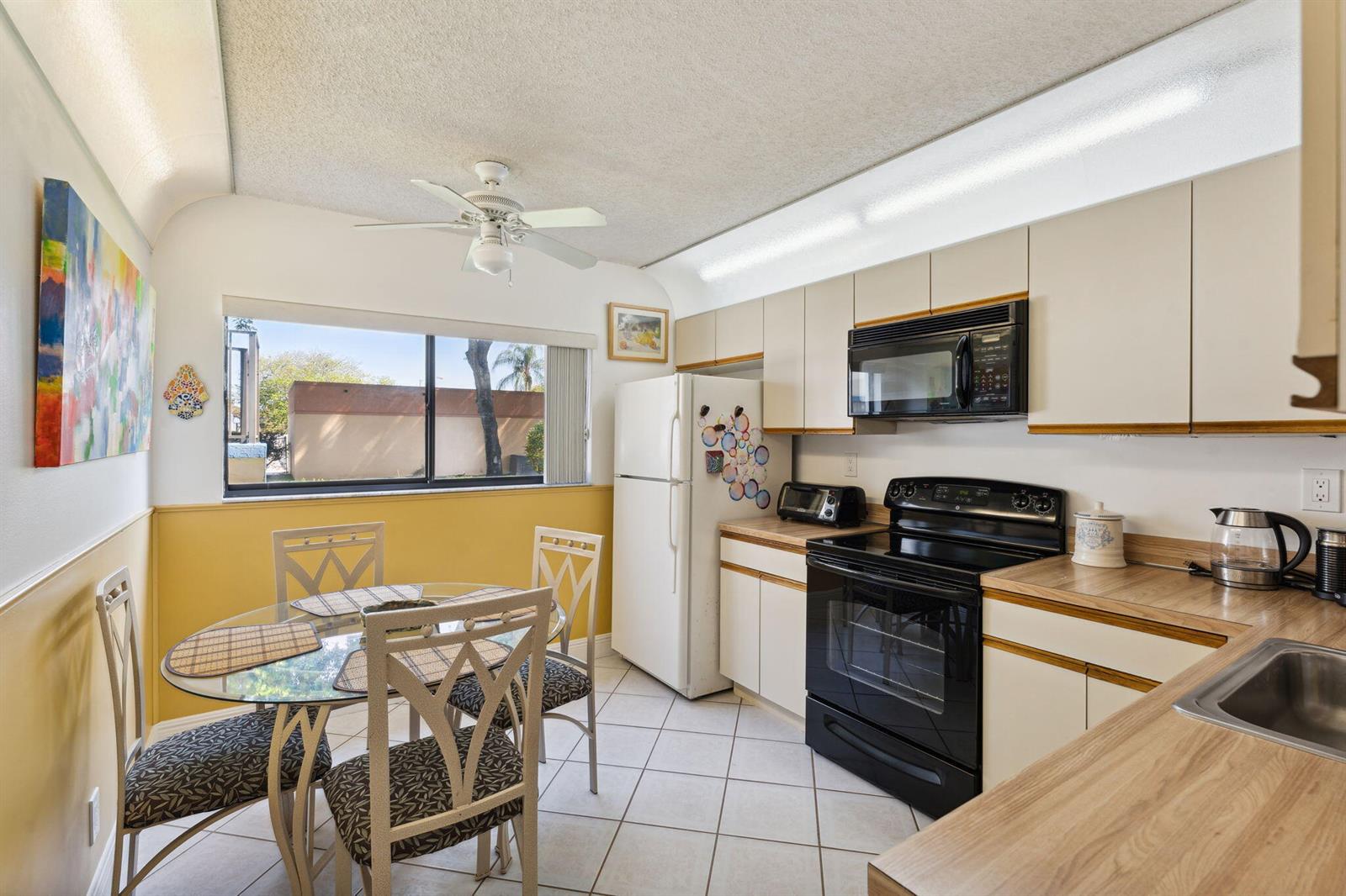 A kitchen with white cabinets, wood-look countertops, black appliances, and a small dining area — 15301 Pembridge Avenue # 43, Delray Beach FL 33484, DELRAY BEACH, FL