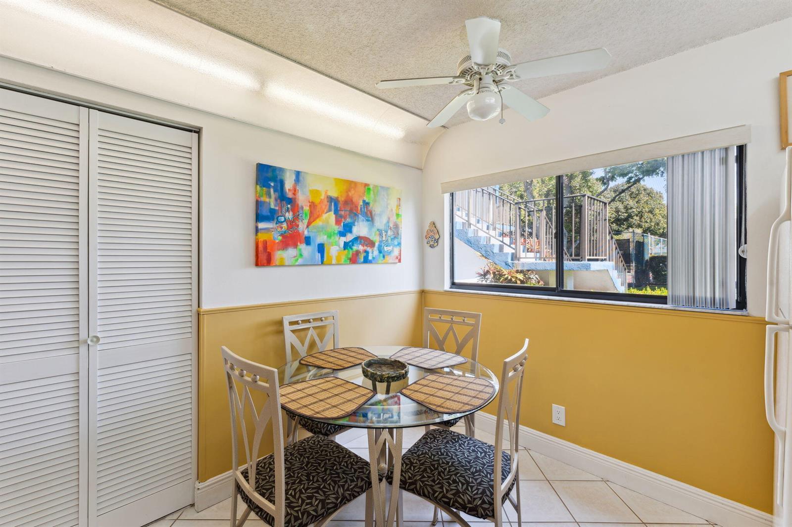 A dining area features a glass table, four chairs, yellow wainscoting, and a window view — 15301 Pembridge Avenue # 43, Delray Beach FL 33484, DELRAY BEACH, FL