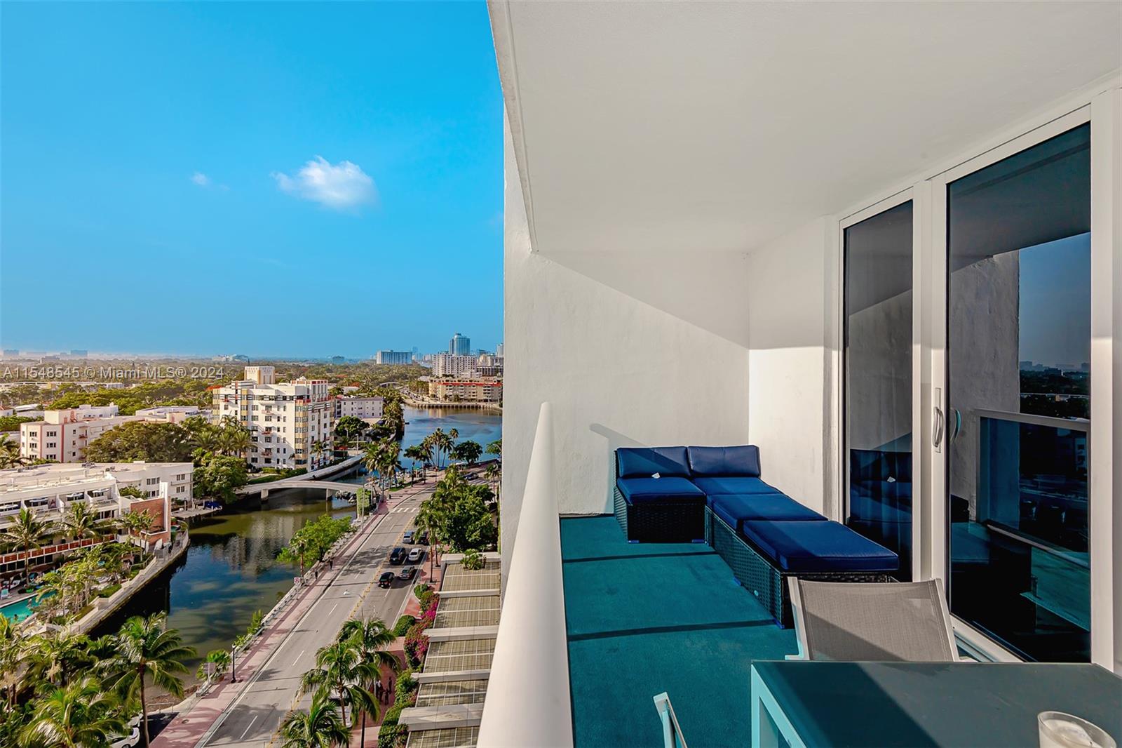 A balcony with blue outdoor furniture overlooks a canal, a road, and city buildings — 2301 Collins Ave # 1230, Miami Beach FL 33139, MIAMI BEACH, FL