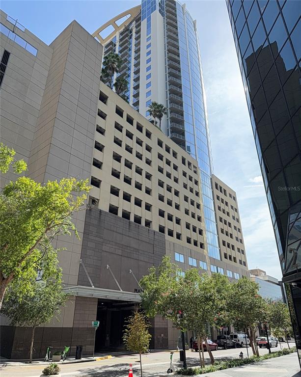 A tall, modern high-rise building with a parking garage base and glass-walled residential tower — 155 S COURT AVENUE UNIT 1104, ORLANDO, FL