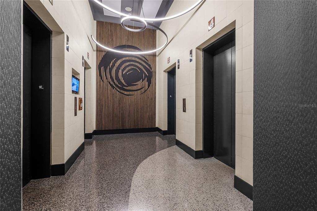 An elevator lobby features black doors, light-colored tiled walls, and a modern circular light fixture — 155 S COURT AVENUE UNIT 1104, ORLANDO, FL