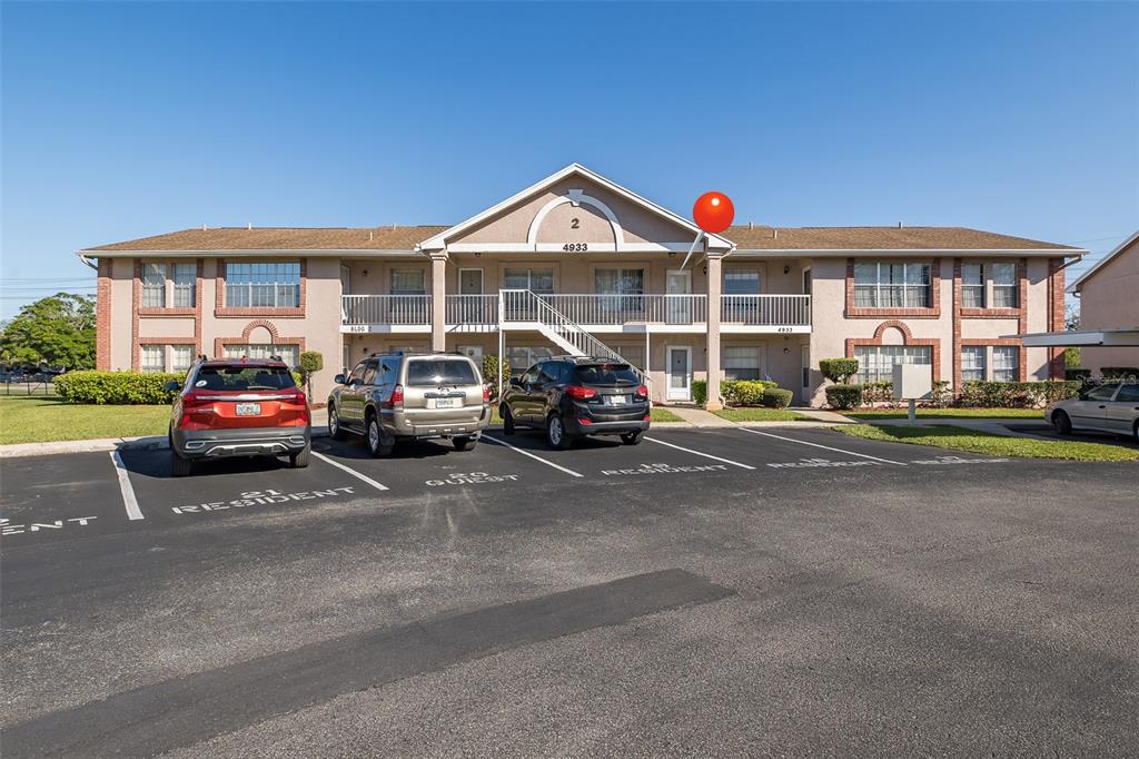 A two-story apartment building with a parking lot in the foreground and a red marker — 4933 MYRTLE OAK DRIVE UNIT 23, NEW PORT RICHEY, FL