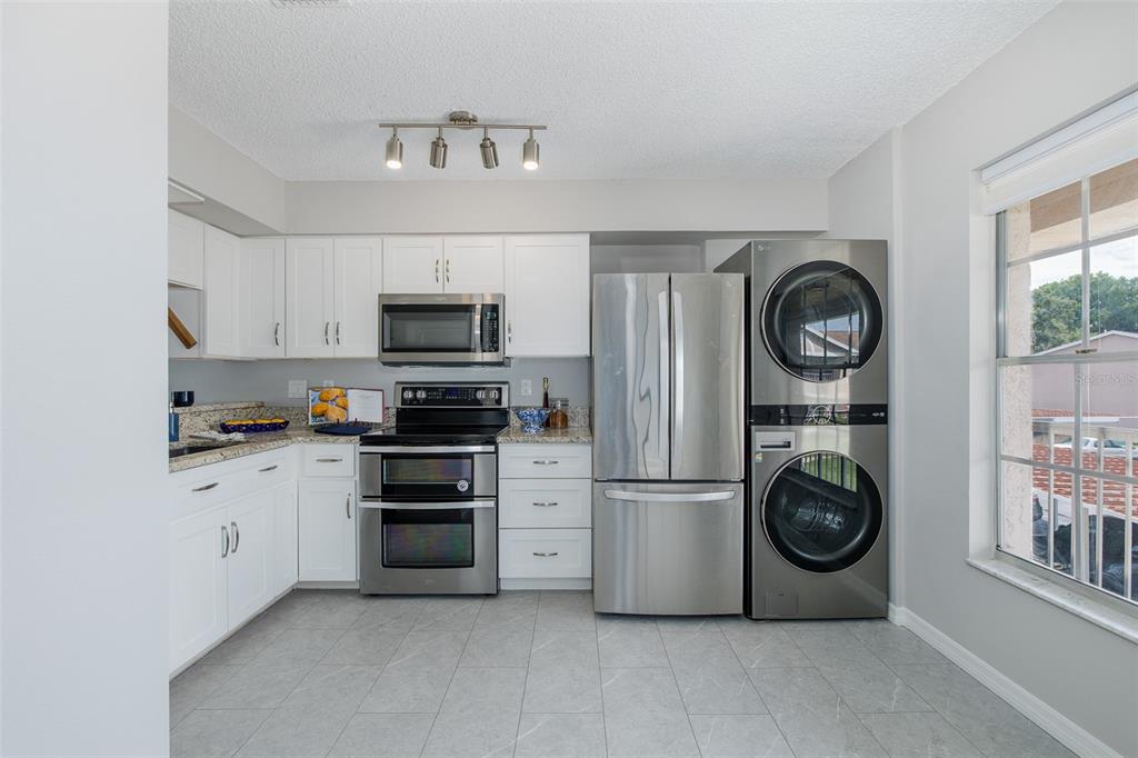 A kitchen features white cabinets, stainless steel appliances, a stacked washer-dryer, and light tile flooring — 4933 MYRTLE OAK DRIVE UNIT 23, NEW PORT RICHEY, FL
